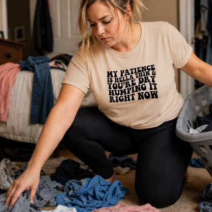 Woman wearing a natural colored t-shirt with My patience is hella thin...text sorting laundry in a room with clothes scattered around