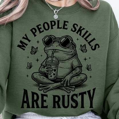 Frog drinking coffee with butterflies and text "My people skills are rusty" on a casual graphic t-shirt