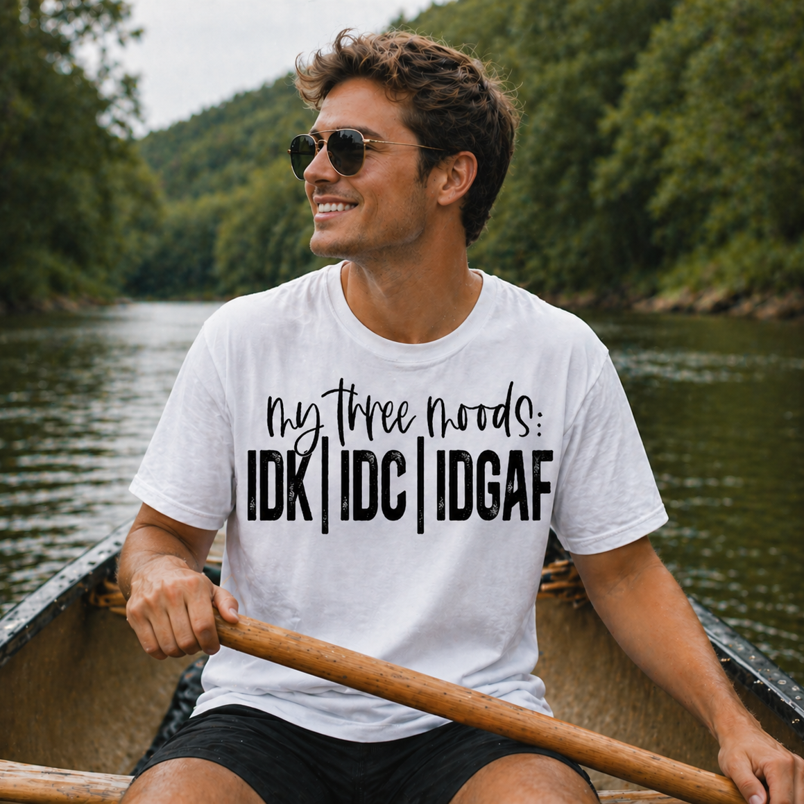 Man in a canoe wearing a white t-shirt with text, surrounded by a natural landscape.