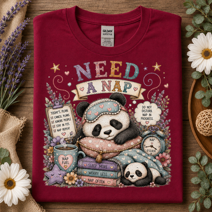 A folded cardinal red t-shirt with a colorful cartoon panda nap graphic, styled on a wooden surface with flowers and burlap.