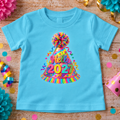 A aqua blue short-sleeve baby t-shirt laid flat on a rustic wooden surface, decorated with a colorful 'Hello 2021' party hat graphic. The shirt is surrounded by festive party decorations including pink paper flowers, gold confetti, and streamers.