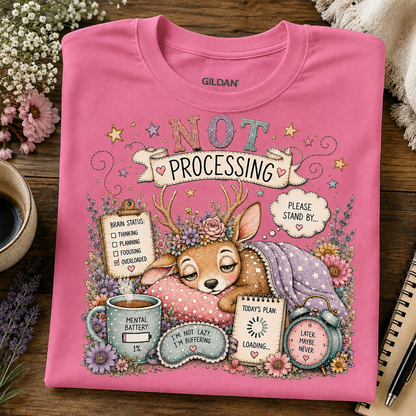 A azalea colored Gildan crewneck sweatshirt with a detailed graphic print of a sleeping deer surrounded by humorous status updates, flowers, and coffee mugs, laid flat on a wooden table.