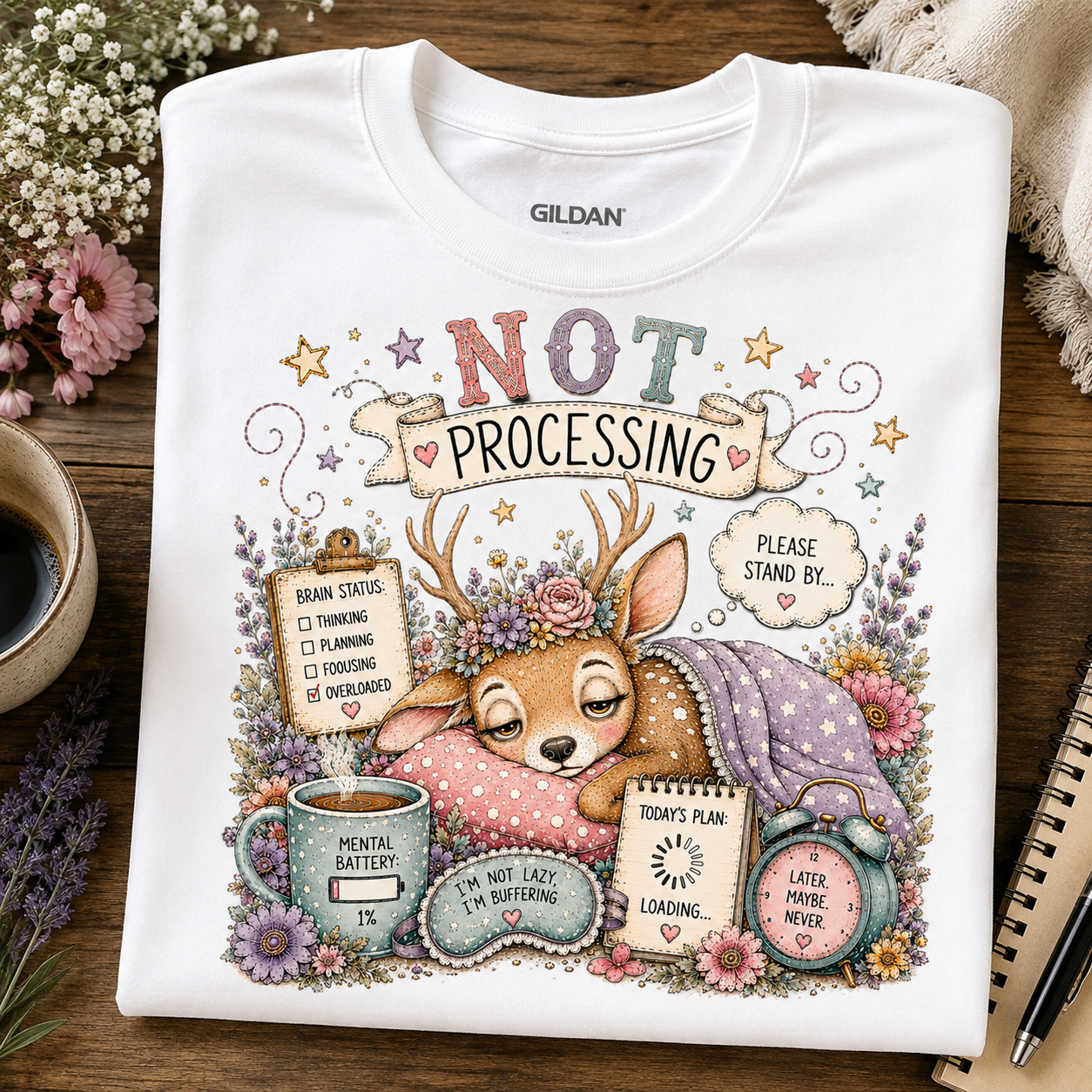A white Gildan crewneck t-shirt laid flat on a rustic wooden table, featuring a detailed graphic of a sleeping deer surrounded by flowers and humorous text like 'NOT PROCESSING' and 'PLEASE STAND BY.'.
