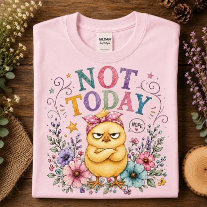 A folded light pink Gildan Softstyle t-shirt with a colorful graphic print of a grumpy yellow chick surrounded by flowers and the text 'NOT TODAY' in multicolored letters, displayed on a rustic wooden background with dried flowers and burlap.