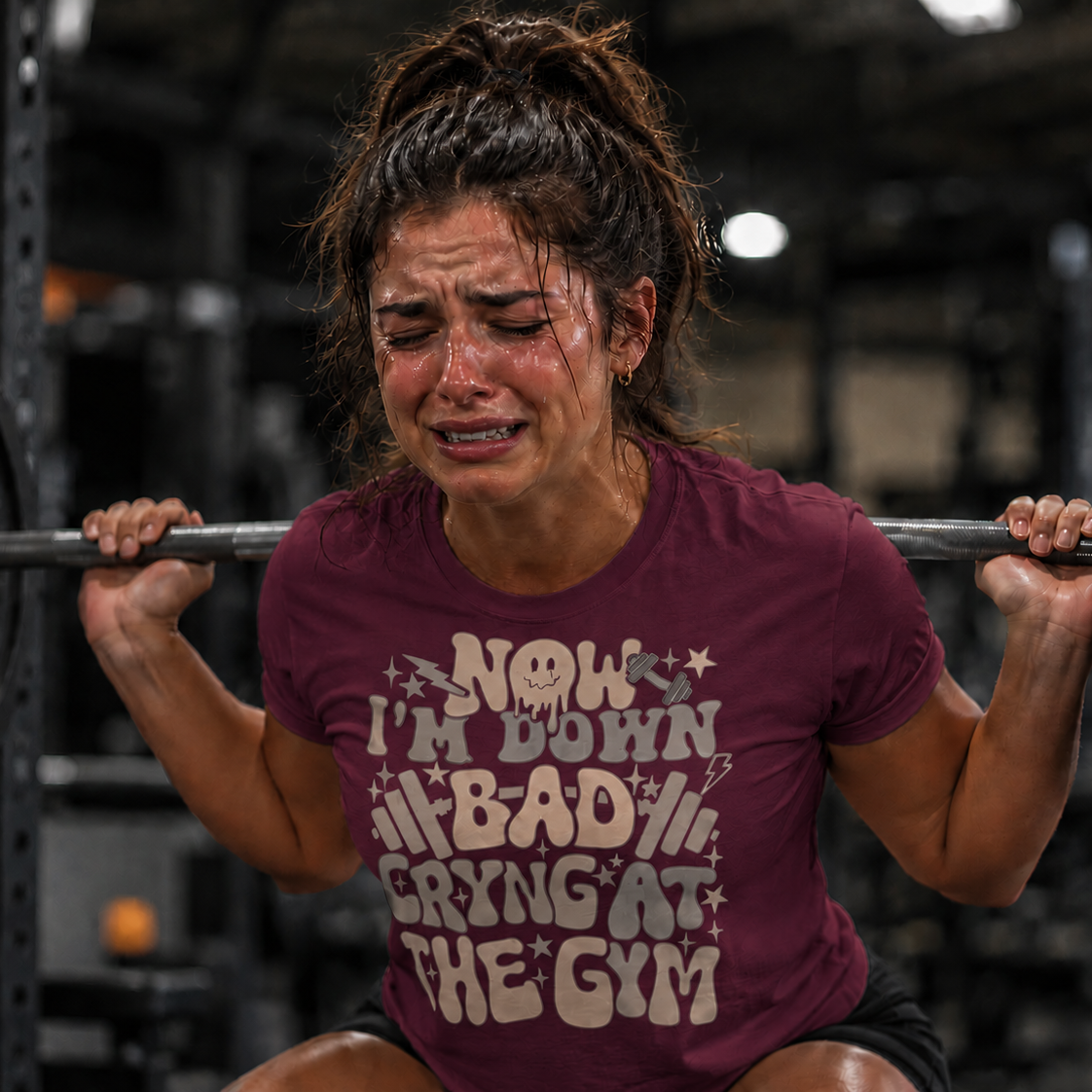 Woman lifting weights with a humorous maroon colored t-shirt in a gym setting