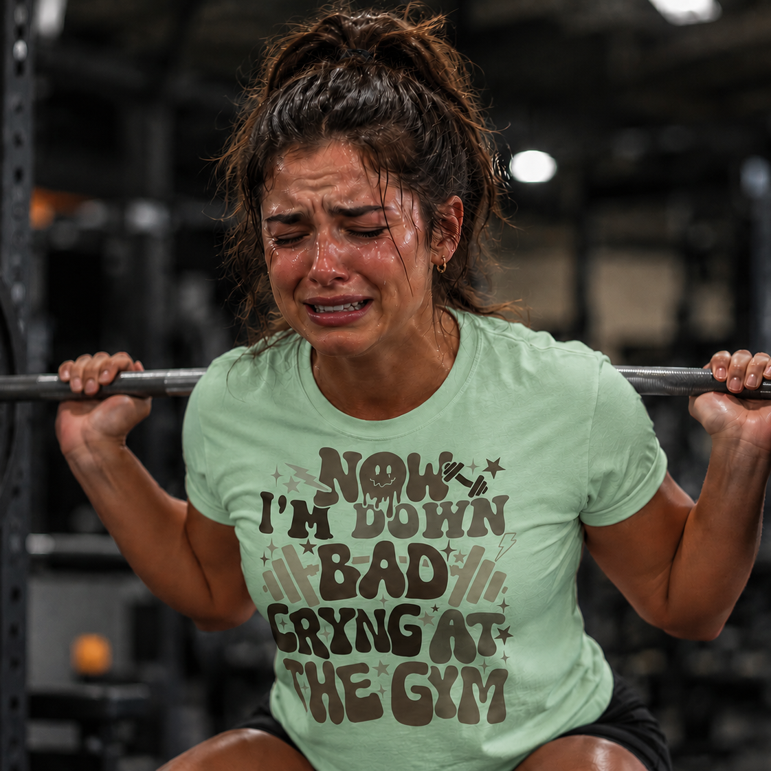 Woman lifting weights with a humorous mint green t-shirt in a gym setting