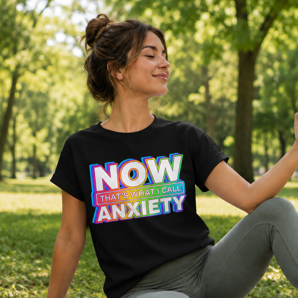 Woman sitting on a yoga mat in a park wearing a black t-shirt with colorful text.