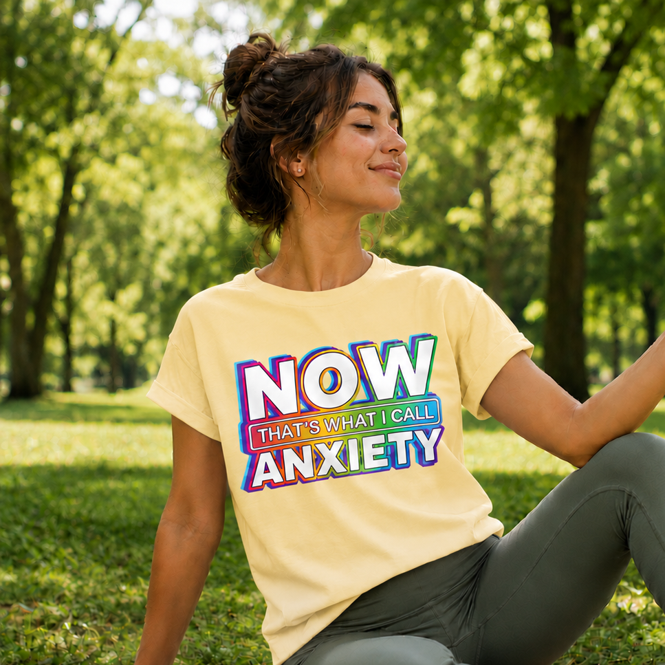 Woman sitting on a yoga mat outdoors wearing a yellow t-shirt with colorful text.