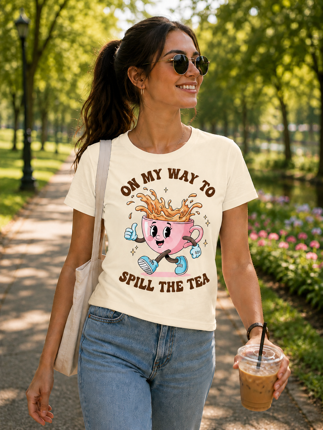 Ivory colored t-shirt with a cartoon pink cup character and text 'On my way to spill the tea' on a denim jacket background.