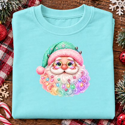 A folded chill blue t-shirt with a colorful graphic of a festive Santa Claus face, styled on a rustic wooden background with holiday decorations.