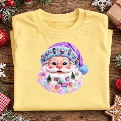 A folded butter yellow t-shirt with a colorful, glittery Santa Claus graphic on the front, displayed on a rustic wooden background decorated with Christmas ornaments, pine branches, and snowflakes.