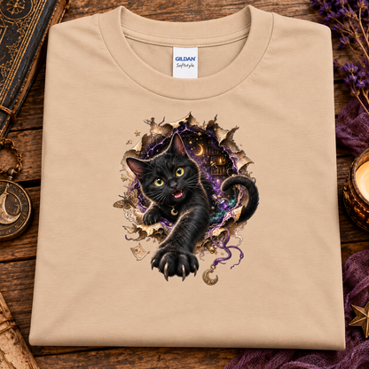 A natural colored graphic T-shirt featuring a 3D black cat with glowing golden-green eyes reaching through a torn magical portal, surrounded by purple mystical energy, crescent moons, stars, and witchy details