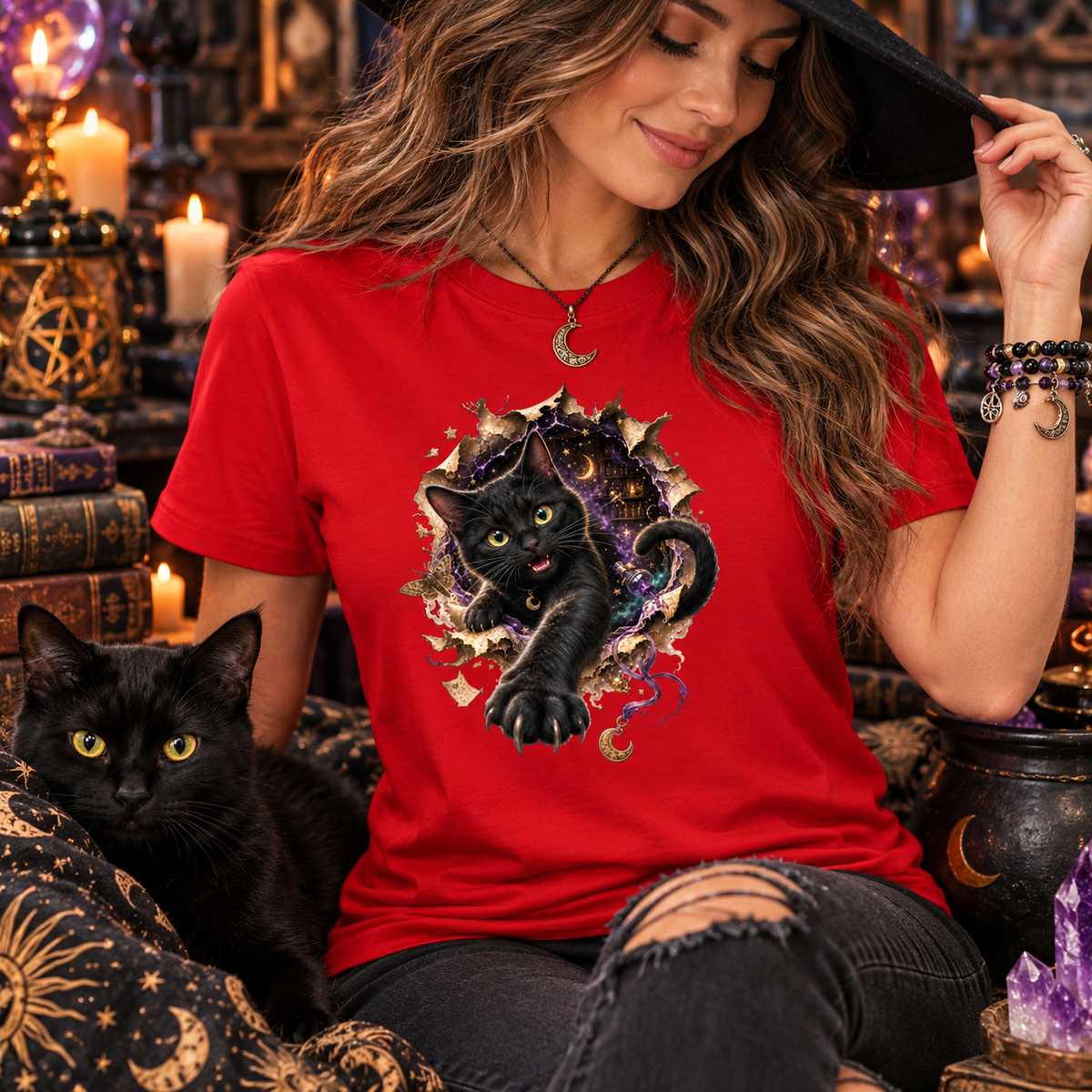 Woman wearing a red graphic T-shirt featuring a 3D black cat with glowing golden-green eyes reaching through a torn magical portal, surrounded by purple mystical energy, crescent moons, stars, and witchy details