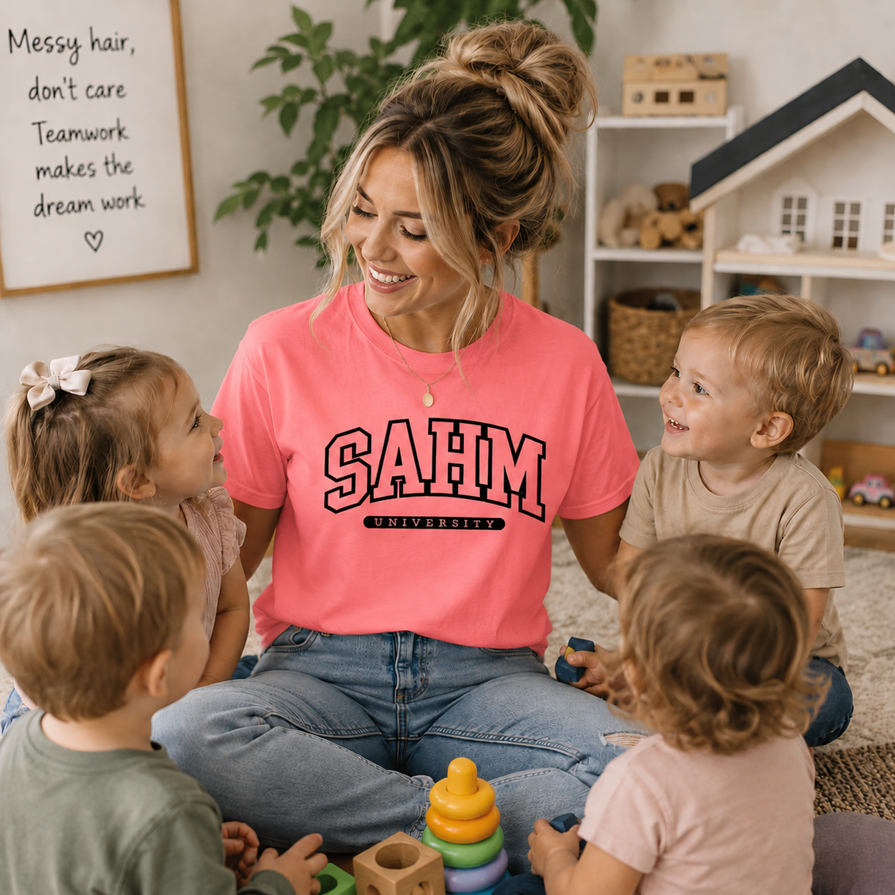 Woman in a pink 'SAHM University' shirt sitting with children in a home setting.