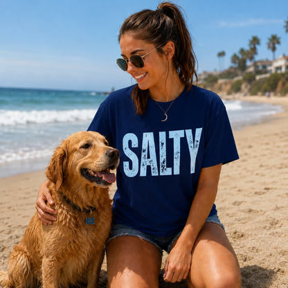 Woman wearing a blue 'SALTY' t-shirt sitting on the beach with a dog.