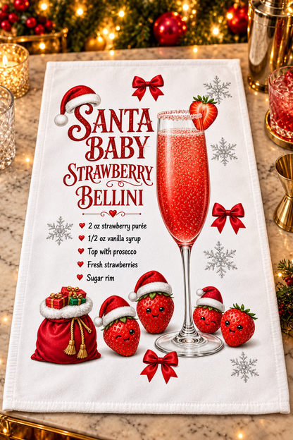 A white kitchen towel with a festive Christmas design featuring the text 'Santa Baby Strawberry Bellini', a large pinkish-red champagne flute, strawberries, red bows, snowflakes, and a red sack of gifts, photographed hanging on a countertop with warm holiday lights in the background.