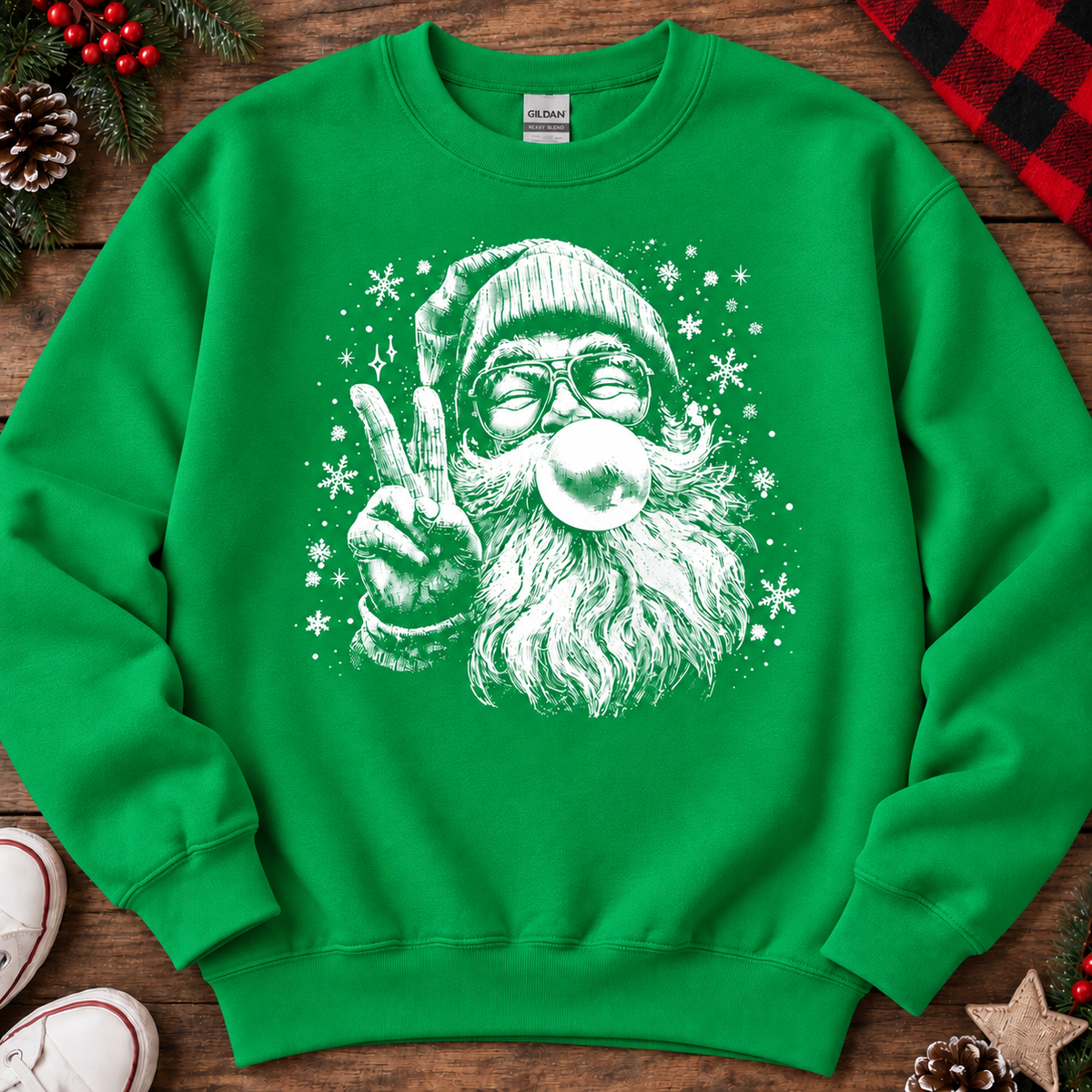 A irish green crewneck sweatshirt featuring a white graphic of a Santa Claus character blowing bubblegum, styled in a flat-lay on a wooden surface with holiday decorations.