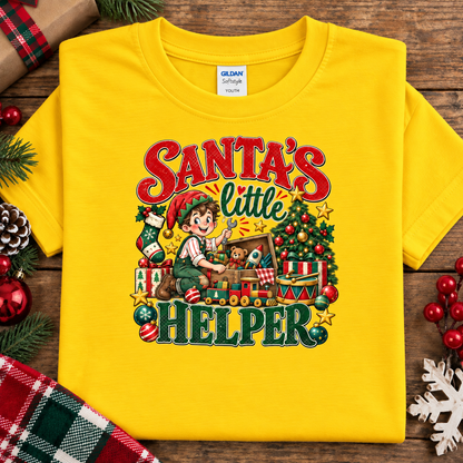 A daisy yellow Gildan Comfort 12x12 short-sleeve t-shirt with a colorful Christmas graphic reading 'Santa's little Helper'. The shirt is displayed flat on a rustic wooden background decorated with pine needles, a pinecone, red berries, and a plaid fabric.