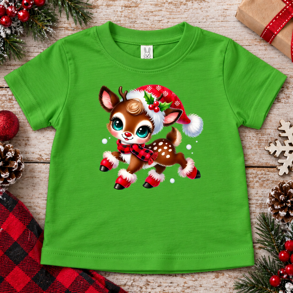 A bright green kids' short-sleeve t-shirt with a cartoon Christmas deer graphic, styled in a flat-lay on a rustic wooden background with holiday decorations.