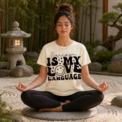 Woman meditating outdoors wearing an ivory colored  t-shirt with 'Sarcasm is my love language' text.
