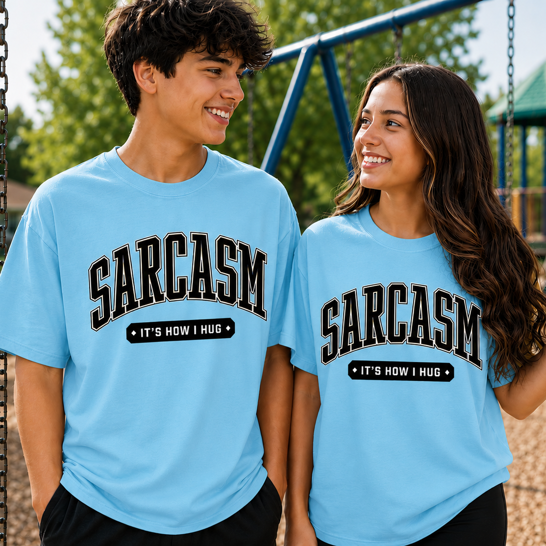Two people wearing light blue t-shirts with 'SARCASM IT'S HOW I HUG' text at a playground.
