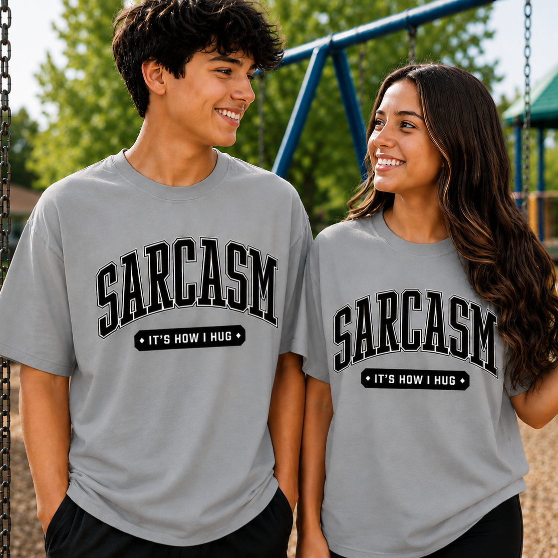 Two people wearing gray t-shirts with 'SARCASM IT'S HOW I HUG' text at a playground.
