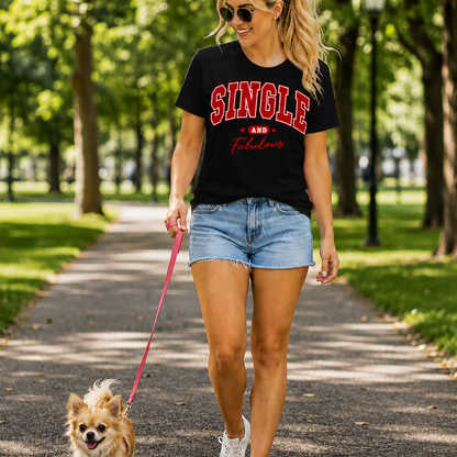 Woman walking a dog on a leash in a park wearing a 'SINGLE AND FABULOUS' black t-shirt.