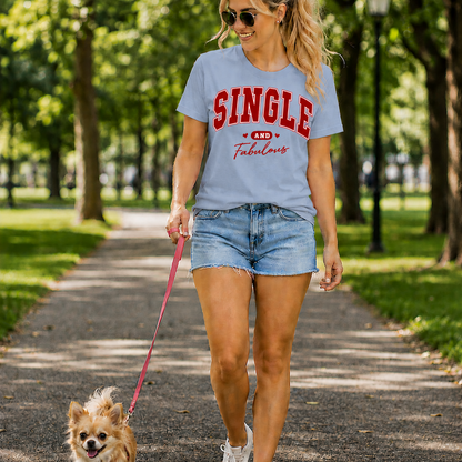 Woman walking a dog on a leash in a park wearing a 'SINGLE AND Fabulous' light blue t-shirt.