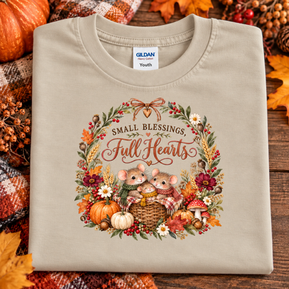 A folded sand colored Gildan Youth t-shirt with a fall-themed mouse graphic, displayed on a rustic wooden background with autumn leaves and pumpkins.