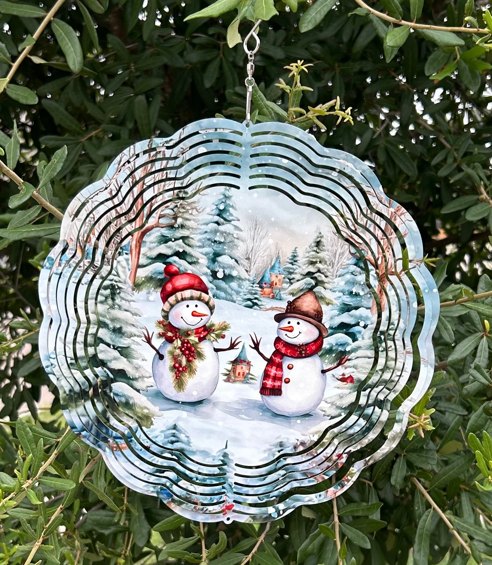 Decorative glass ornament with two snowmen in a winter scene, hanging on a tree.