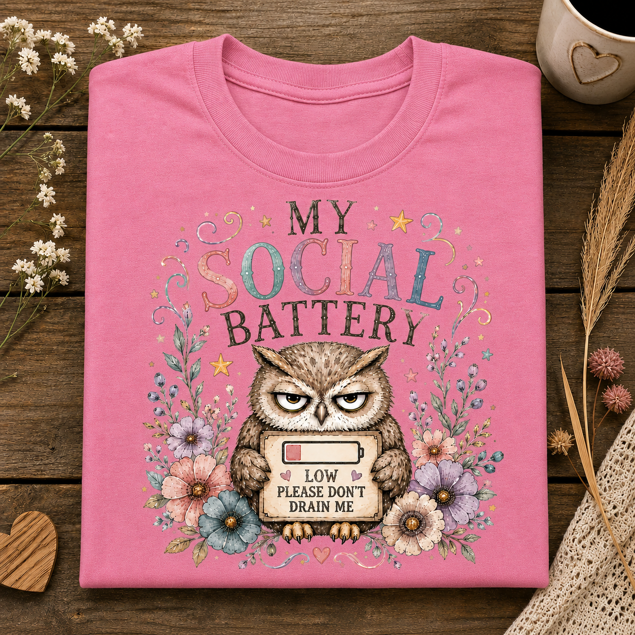 An azalea colored t-shirt with the text MY SOCIAL BATTERY and an owl surrounded by flowers holding a sign with a low meter that says LOW PLEASE DON"T DRAIN ME