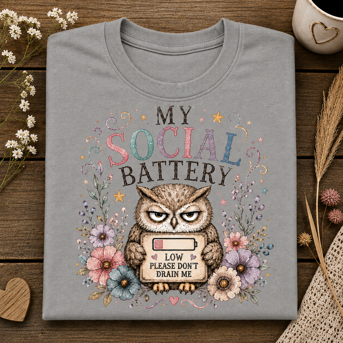A sport grey colored t-shirt with the text MY SOCIAL BATTERY and an owl surrounded by flowers holding a sign with a low meter that says LOW PLEASE DON"T DRAIN ME