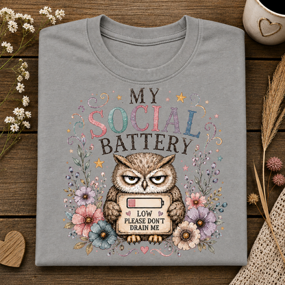 A sport grey colored t-shirt with the text MY SOCIAL BATTERY and an owl surrounded by flowers holding a sign with a low meter that says LOW PLEASE DON"T DRAIN ME