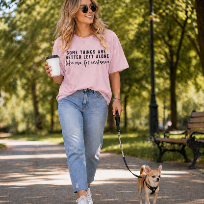 Woman walking a dog in a park wearing a light pink graphic t-shirt with text.