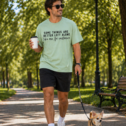 Man walking a dog on a leash in a park, wearing a light green t-shirt with text.