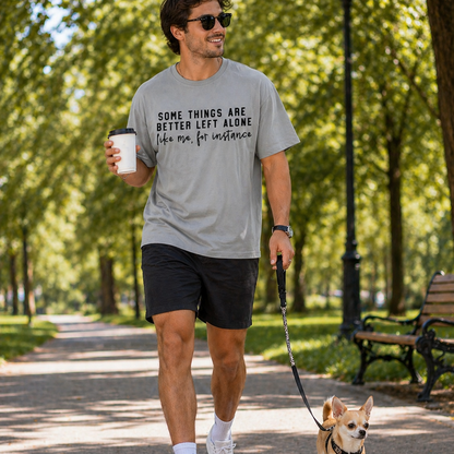 Man walking a dog in a park wearing a graphic t-shirt with text and holding a coffee.