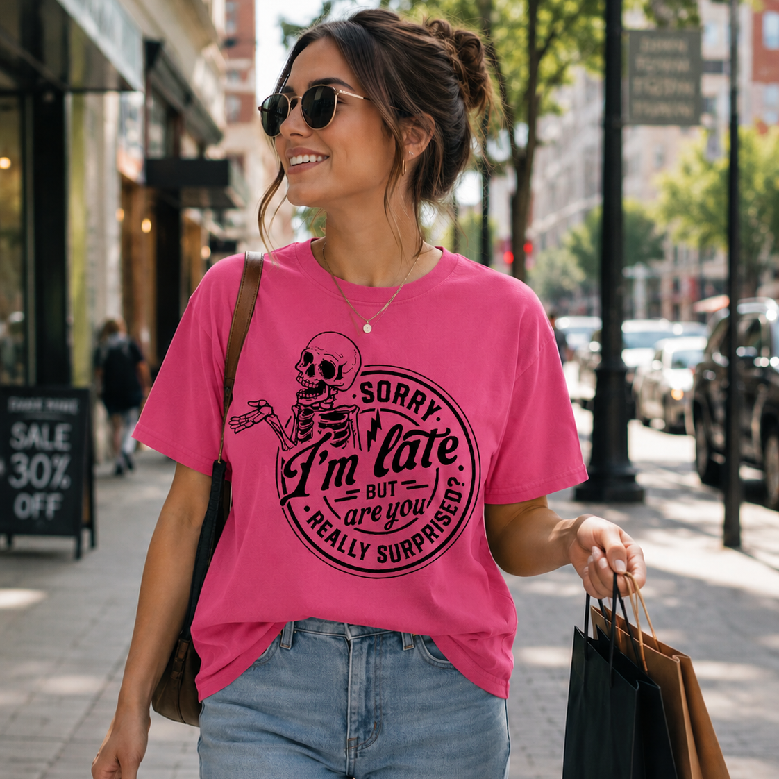 Woman walking down a street wearing a heather heliconia colored white t-shirt with a skeleton graphic and text.