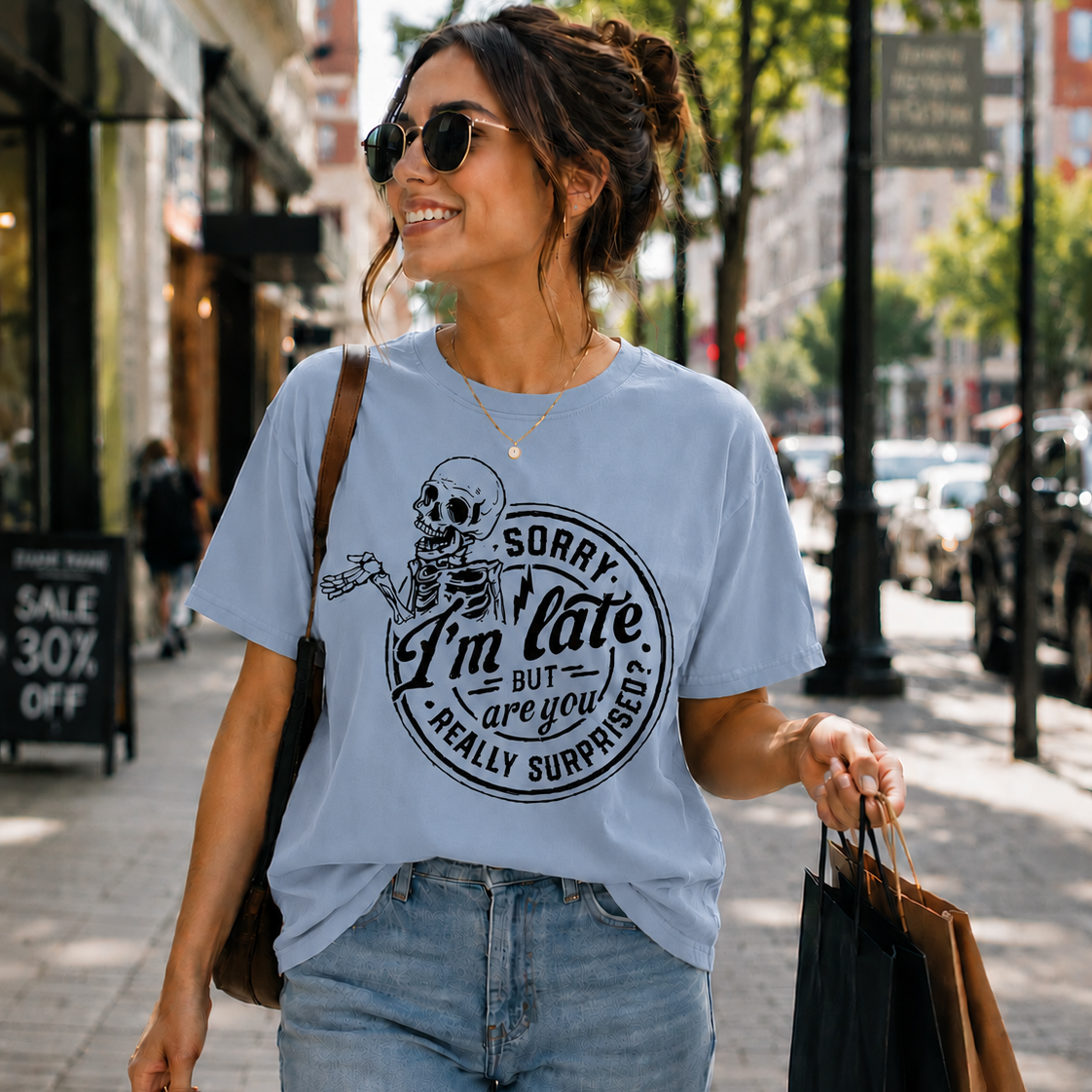 Woman walking down a street wearing a light blue colored t-shirt with a skeleton graphic and text.