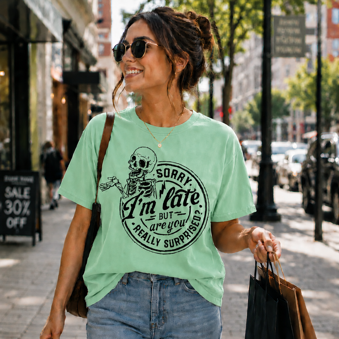Woman walking down a street wearing a mint green colored t-shirt with a skeleton graphic and text.