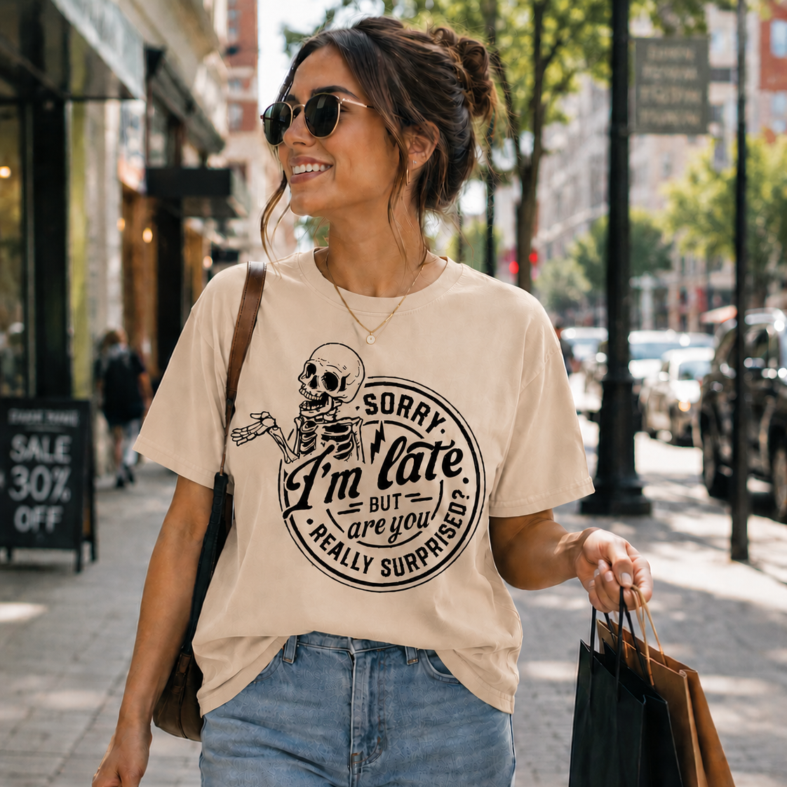 Woman walking down a street wearing a natural colored t-shirt with a skeleton graphic and text.