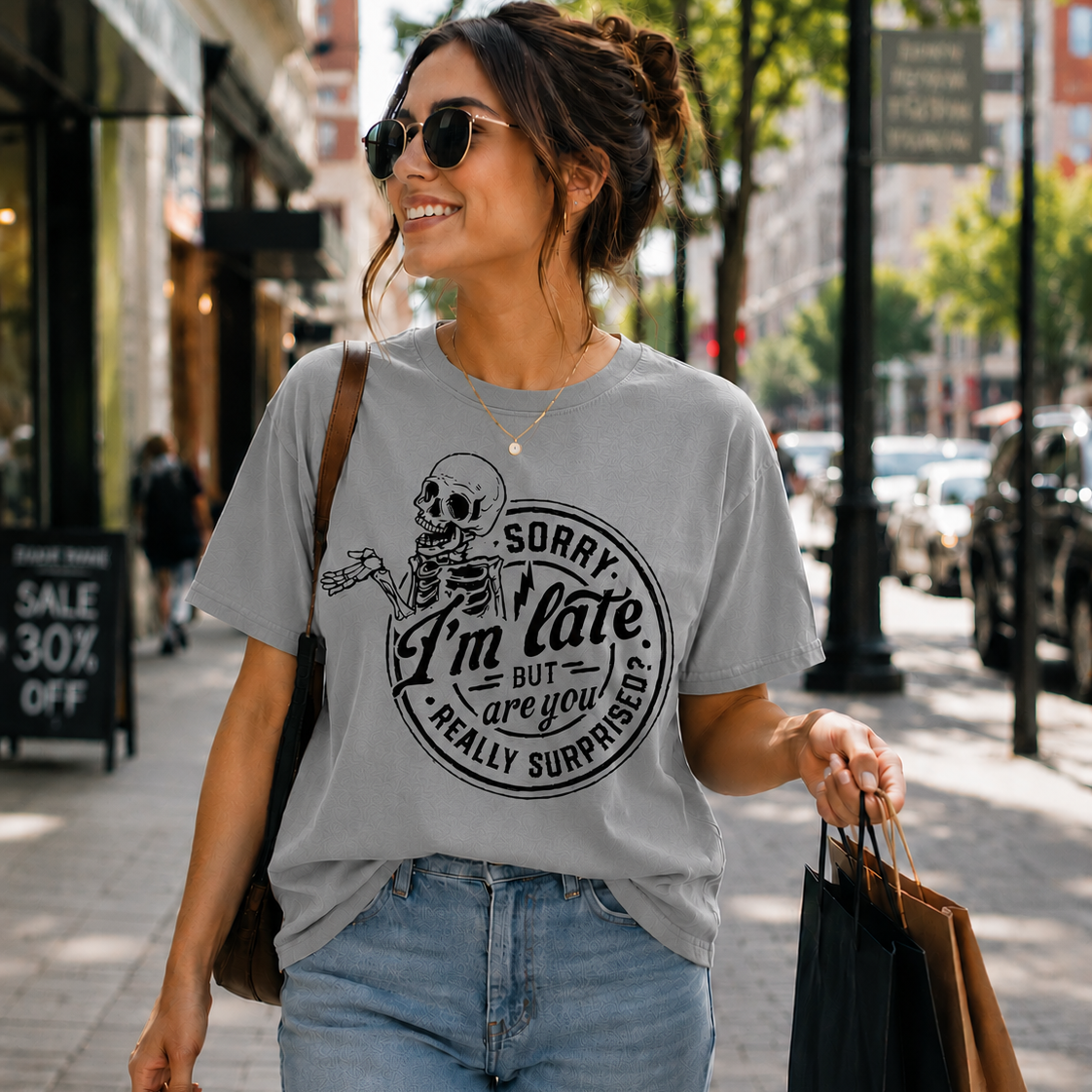 Woman walking down a street wearing a sport grey colored t-shirt with a skeleton graphic and text.