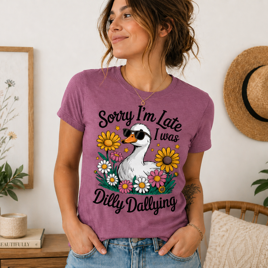 Woman wearing a heather berry t-shirt with a graphic and text, standing in a room with decor.
