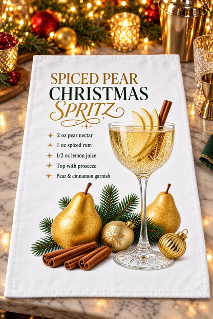A white kitchen towel printed with a festive Christmas spiced pear spritz recipe and a graphic of a filled coupe glass with pear slices, cinnamon sticks, pears, pine branches, and gold ornaments. The towel is styled on a marble surface with blurred holiday lights and ornaments in the background.
