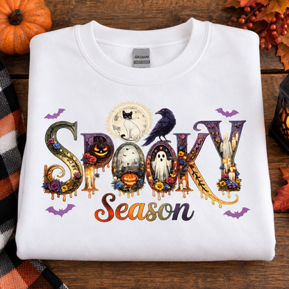 A folded white Gildan t-shirt with a colorful 'Spooky Season' graphic print, styled on a rustic wooden background with pumpkins and autumn leaves.