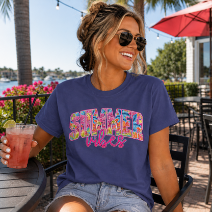 Woman wearing a metro blue colored  'Summer vibes' shirt outdoors with a drink.