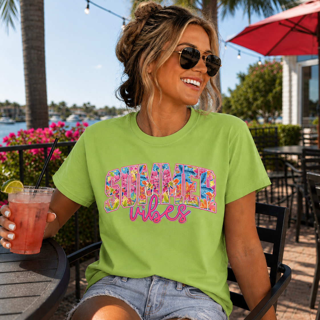 Woman wearing a lime colored 'Summer Vibes' t-shirt holding a drink outdoors.