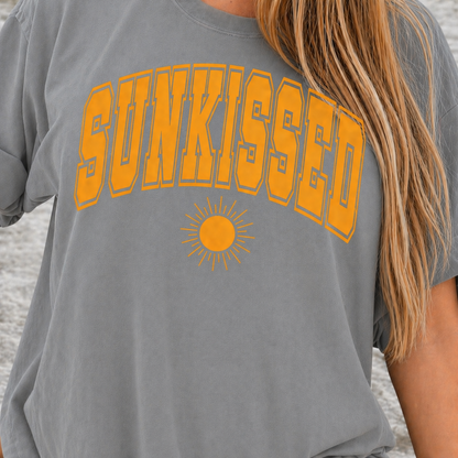 Sport gray t-shirt with 'SUNKISSED' in orange and a sun graphic on a beach.