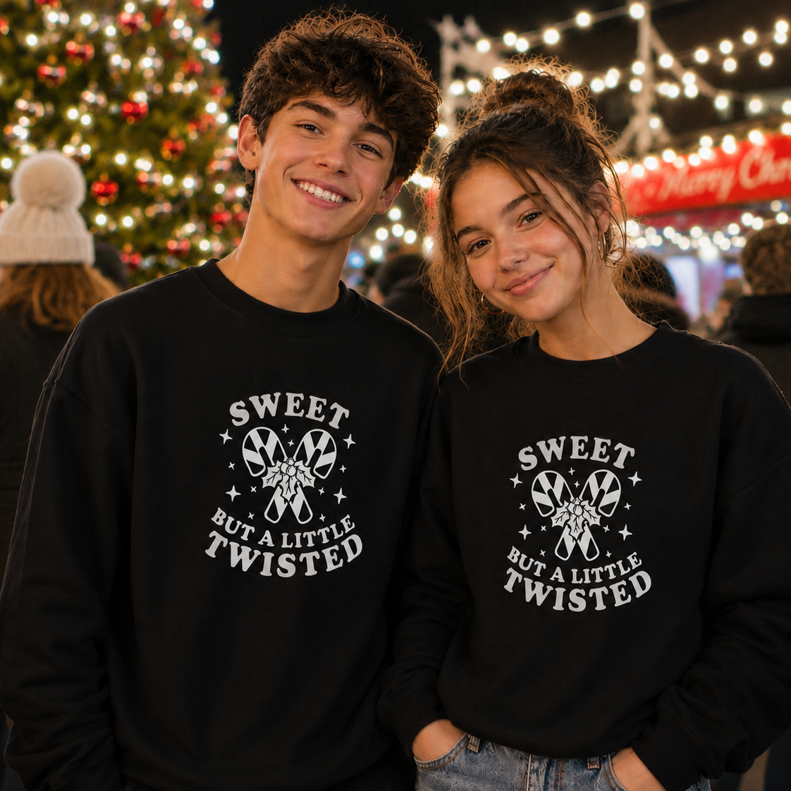 Two people wearing black sweatshirts with a Christmas tree and festive lights in the background.