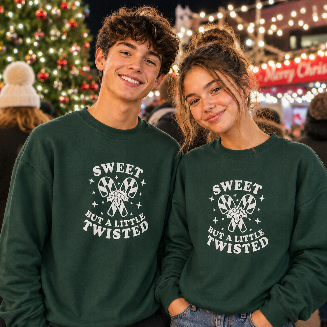 Two people wearing green sweatshirts with a Christmas-themed design in a festive outdoor setting.