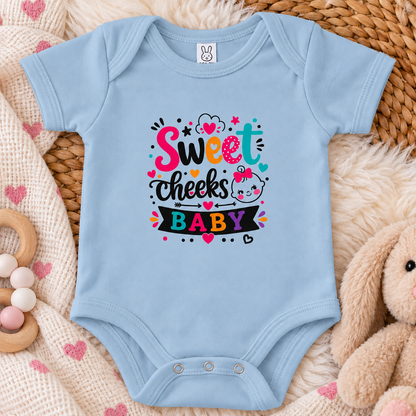 A light blue colored graphic onesie design with the words 'Sweet cheeks BABY' in playful hand-lettered typography, surrounded by hearts, stars, dots, and a cartoon baby face with a pink bow on a white background.